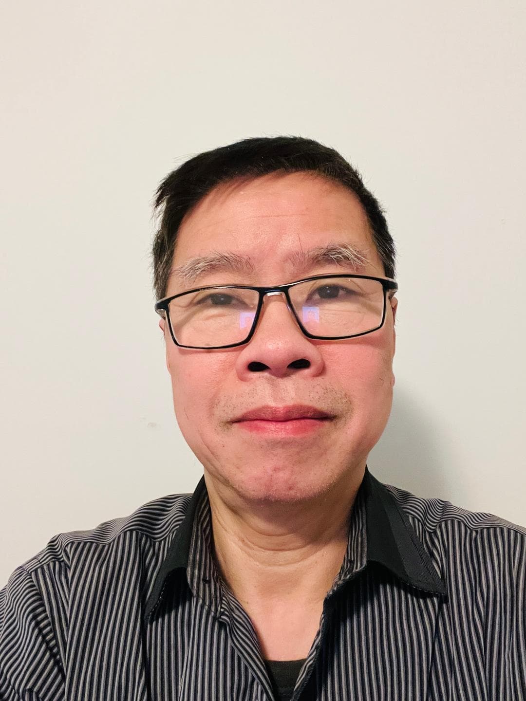 Middle-aged East Asian man with black glasses and short hair wearing a dark striped shirt.